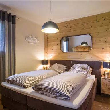 Ein gemütliches Schlafzimmer mit einem Doppelbett und Holzwänden. Weiche Bettwäsche und sanfte Beleuchtung sorgen für eine einladende Atmosphäre.