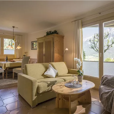 Ein gemütliches Wohnzimmer mit hellen Möbeln und großen Fenstern, die den Blick auf die Berge ermöglichen. Der Raum ist warm und einladend, ideal zum Entspannen.