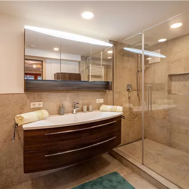 Ein modernes Badezimmer mit einer großen Dusche und einem eleganten Waschtisch. Die Wände sind mit beige Fliesen gestaltet und es gibt einen weichen, blauen Teppich.