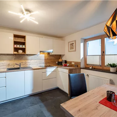 Eine moderne Küche mit weißen Schränken und Holzdetails. Ein Tisch mit Stühlen und dekorativen Elementen lädt zum Essen ein.