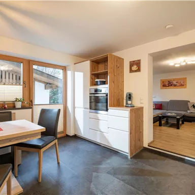 Eine moderne Küche mit einem Esstisch und Stühlen. Im Hintergrund ist ein Wohnzimmer sichtbar, das gemütlich eingerichtet ist.