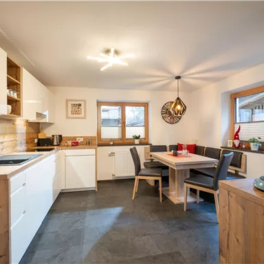 Eine moderne Küche mit Holz- und Weißtönen. Es gibt einen Essbereich mit einem Tisch und Stühlen sowie ausreichend Tageslicht.