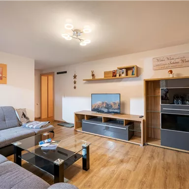 Ein gemütliches Wohnzimmer mit einer modernen Couch und einem Fernseher. Der Raum ist hell und bietet eine einladende Atmosphäre.