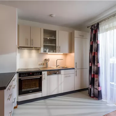 Eine moderne Küche mit hellen Möbeln und einer großen Fensterfront. Der Raum ist gut beleuchtet und einladend.