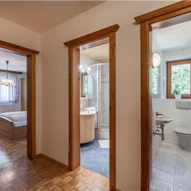 Ein Flur mit zwei offenen Türen zu Badezimmer und Schlafzimmer. Der Raum hat helle Wände und Holzverkleidung.