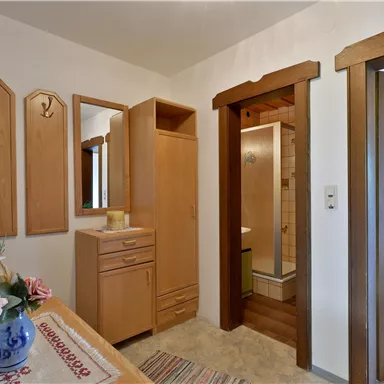 Ein Eingangsbereich mit hölzernen Möbeln und Spiegeln. Auf dem Tisch steht eine Vase mit Blumen und der Raum hat eine gemütliche Atmosphäre.