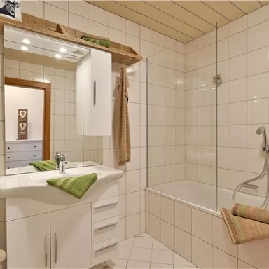 Ein modernes Badezimmer mit hellen Fliesen und einer Badewanne. Grüne Handtücher und Accessoires verleihen eine frische Note.