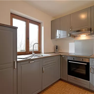 Eine moderne Küche mit grauen Schränken und eleganten Geräten. Das Licht von den Fenstern sorgt für eine helle und einladende Atmosphäre.