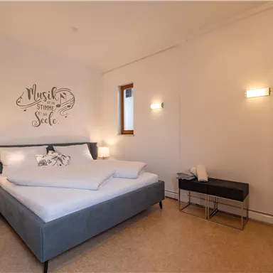 Ein modernes Schlafzimmer mit einem großen Bett und stilvollen Möbeln. Die Wände sind hell und eine dekorative Schriftart verleiht dem Raum Charakter.