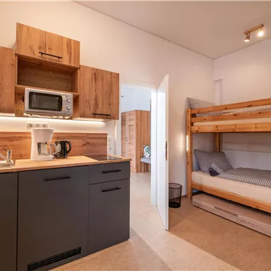 Eine moderne Küche mit Holzschränken und einer Mikrowelle. Im Raum befindet sich ein Etagenbett und eine gemütliche Atmosphäre.