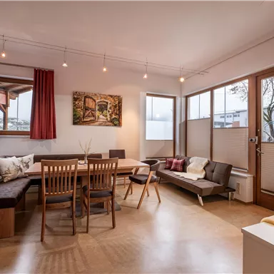 Ein modernes Wohnzimmer mit einem Holztiertisch und bequemen Sitzgelegenheiten. Große Fenster lassen viel Licht herein und schaffen eine einladende Atmosphäre.