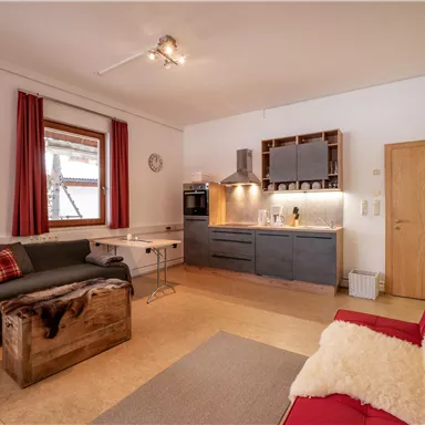 Eine moderne Wohnküche mit einem gemütlichen Sofa und einem klaren Essbereich. Die warmen Farben und die Holzdetails schaffen eine einladende Atmosphäre.