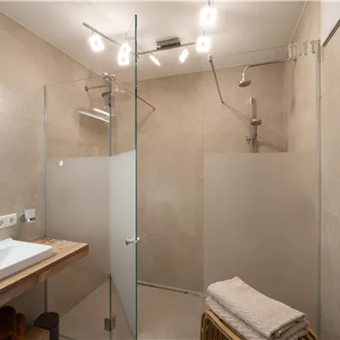Ein modernes Badezimmer mit einer gläsernen Dusche und einem eleganten Waschbecken. Der Raum hat eine helle, neutrale Farbgestaltung und angenehme Beleuchtung.