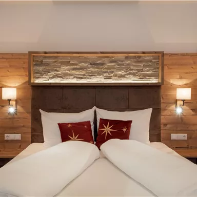 Ein modernes Schlafzimmer mit einem Holz-Nachtisch und einer Steinwand hinter dem Bett. Die Betten sind mit weißen Decken und roten Kissen dekoriert.