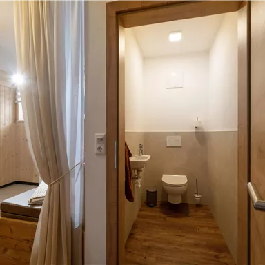 Ein modernes Badezimmer mit einem WC und hellem Licht. Die Wände sind in neutralen Farben gehalten und der Boden ist aus Holz.