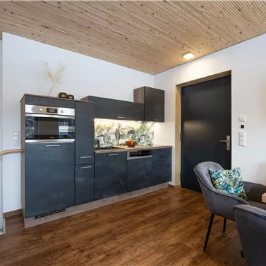 Eine moderne Küche mit schwarzen Möbeln und Holzdecke. Der Raum ist hell und freundlich gestaltet, mit einem gemütlichen Esstisch.