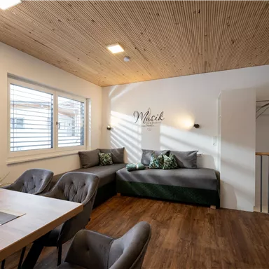 Ein modernes Wohnzimmer mit einem gemütlichen Sofa und einem Tisch. Die Wände sind hell und die Holzdecke sorgt für eine warme Atmosphäre.