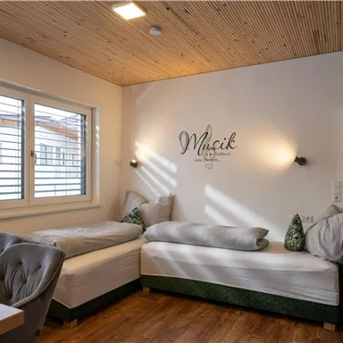 Ein gemütliches Zimmer mit zwei Einzelbetten und einem Holzboden. Die Wände sind hell, und ein Fenster lässt viel Tageslicht herein.