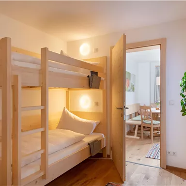Ein gemütliches Zimmer mit einem Etagenbett aus hellem Holz. Im Hintergrund sind ein Tisch und Stühle sichtbar.
