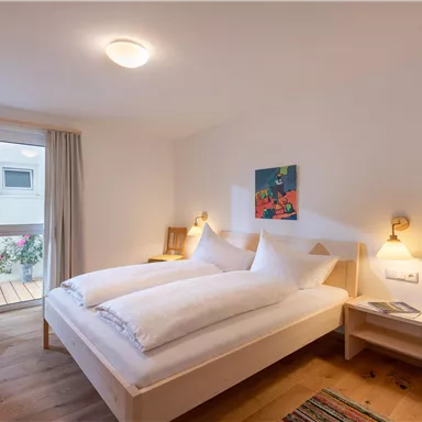 Ein gemütliches Zimmer mit einem Doppelbett und modernem Holzdesign. Große Fenster sorgen für viel Tageslicht.