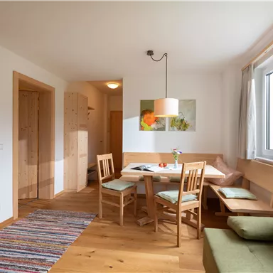 Ein gemütlicher Wohnraum mit einem Essbereich und Holzfußboden. Die Wände sind hell und das Fenster lässt viel natürliches Licht herein.