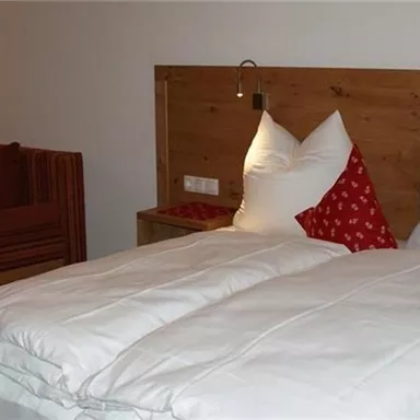 Ein modernes Schlafzimmer mit einem Doppelbett und zwei großen Kissen. Im Hintergrund befindet sich eine rote Couch.