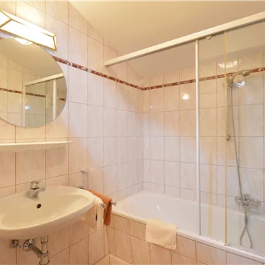 Ein helles Badezimmer mit einer Badewanne und einer Dusche. Der Spiegel und die sanitären Anlagen sind modern und gut gepflegt.