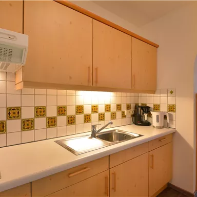 Eine modern eingerichtete Küche mit Holzschränken und einem hellen Fliesenspiegel. Im Hintergrund ist ein gemütlicher Wohnbereich sichtbar.