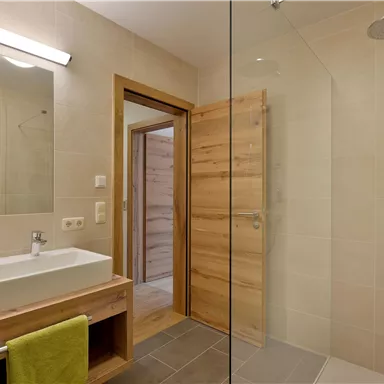 A modern bathroom with a shower and a washbasin. The walls are light, and the wood decor creates a warm atmosphere.