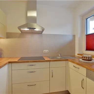A modern kitchen with bright cabinets and wooden countertops. The window has red blinds and there is a cake on the countertop.