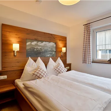 A modern bedroom with a double bed and elegant wooden cladding. Large windows provide plenty of daylight and a pleasant atmosphere.