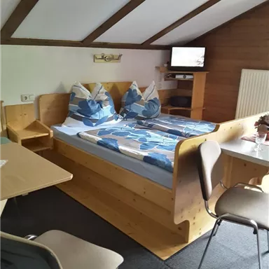 Ein gemütliches Schlafzimmer mit einem Doppelbett, stimmungsvollem Dekor und einem Fernseher. Es gibt auch einen Tisch und Stühle zum Sitzen.