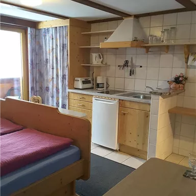 Eine gemütliche Ferienwohnung mit einem Bett, einer kleinen Küchenzeile und einem Tisch. Große Fenster lassen viel Licht herein und bieten einen Blick nach draußen.