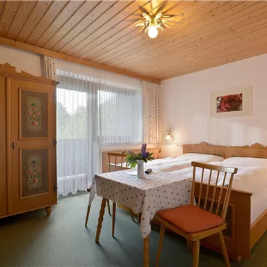 Ein gemütliches Zimmer mit einem Doppelbett und einem Holzschrank. Der Tisch und die Stühle schaffen eine einladende Atmosphäre.