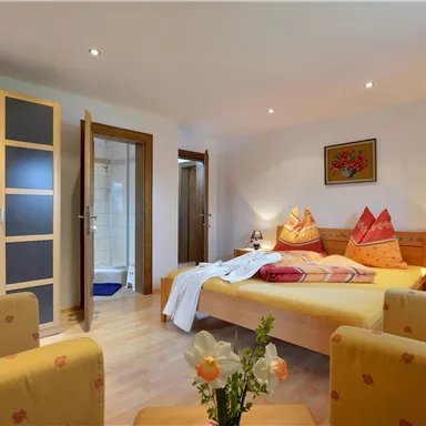 Ein gemütliches Zimmer mit einem Doppelbett und zwei bequemen Sesseln. Die Ausstattung umfasst eine moderne Dusche und eine angenehme Beleuchtung.