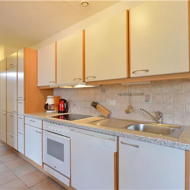 Eine moderne Küche mit hellen Schränken und einer gemütlichen Atmosphäre. Sie ist ausgestattet mit einem Waschbecken, Herd und verschiedenen Küchengeräten.