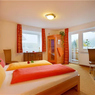 A cozy bedroom with two beds and colorful pillows. There is a small dining area and windows overlooking the outdoors.