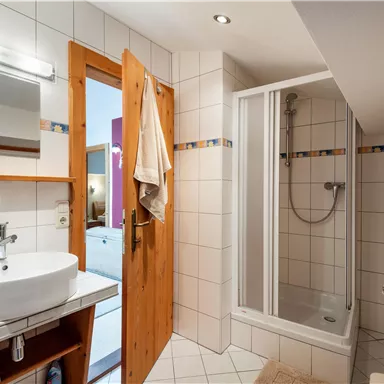 A modern bathroom with a shower, a sink, and bright tiles. The wooden door and the mirror give the room a cozy atmosphere.