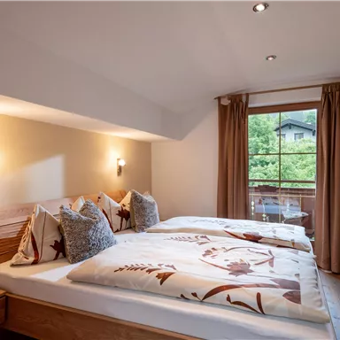 A cozy bedroom with two beds and decorative pillows. The window offers a view of the green surroundings.