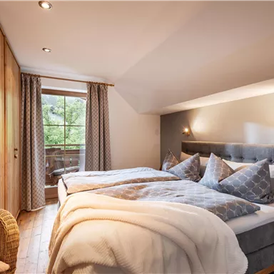 A cozy bedroom with two beds and soft pillows. Large windows offer a view of the greenery.