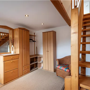 A bright hallway with wooden furniture and a staircase. There is a mirror, a wardrobe, and a cozy armchair.