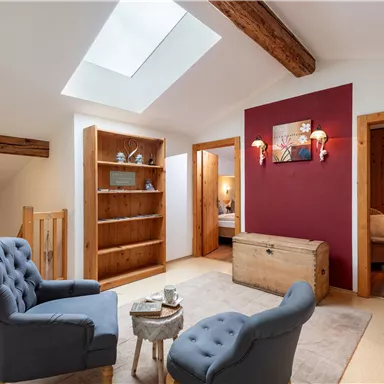 A cozy living area with two blue armchairs and a table. On the wall is a red accent wall and a bookshelf.