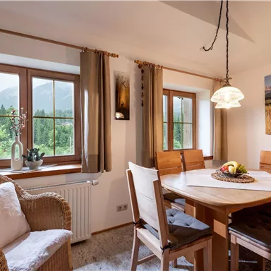 A cozy dining area with wooden chairs and a table. Large windows offer a view of the landscape and provide plenty of daylight.