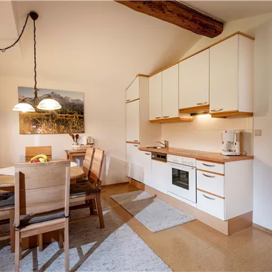 A modern kitchen with a dining table and chairs. The walls are light and there is nice lighting.