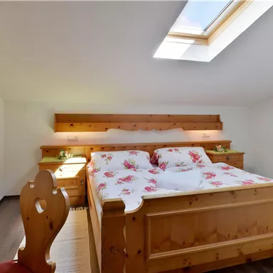 Ein gemütliches Schlafzimmer mit einem großen Holzbett und hellen Linens. Das Zimmer hat ein Dachfenster, das viel Tageslicht hereinlässt.