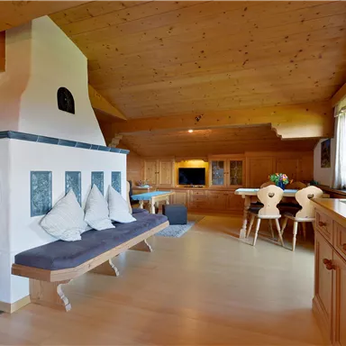 Ein gemütlicher Wohnraum mit Holzwänden und einem modernen Kamin. Der Raum verfügt über eine Sitzbank, einen Esstisch und große Fenster, die viel Licht hereinlassen.