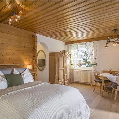 Ein gemütliches Zimmer mit einem Doppelbett und Holz details. Der Raum hat einen Esstisch neben einem Fenster mit Blick auf die Natur.