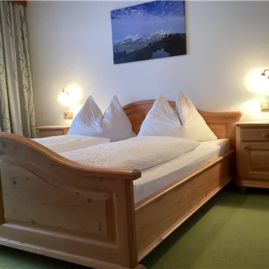 Ein gemütliches Schlafzimmer mit einem Doppelbett aus Holz und zwei Kissen. An der Wand hängt ein Bild von einer Berglandschaft.