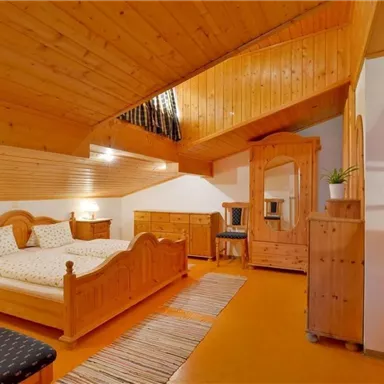 A cozy bedroom with wooden furniture and two beds. The room has a warm atmosphere and is well-lit.