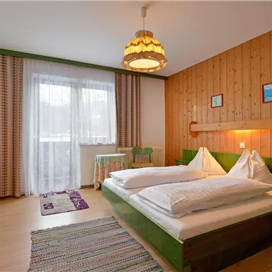 Ein gemütliches Schlafzimmer mit einem Doppelbett und Holzverkleidung. Das Zimmer ist hell und freundlich, mit einem Fenster, das Tageslicht hereinlässt.